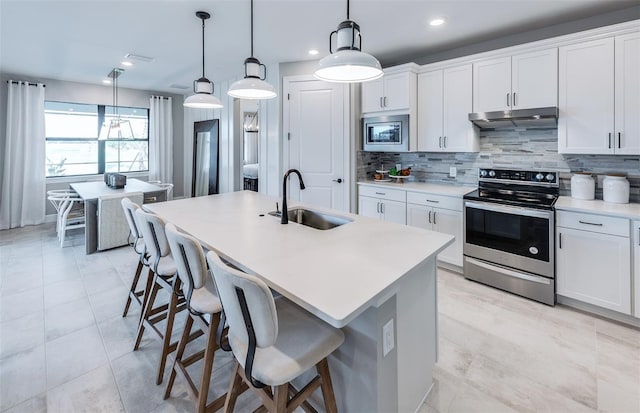 kitchen with a breakfast bar area, stainless steel appliances, backsplash, a sink, and under cabinet range hood