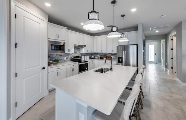 kitchen featuring tasteful backsplash, visible vents, stainless steel appliances, under cabinet range hood, and a sink