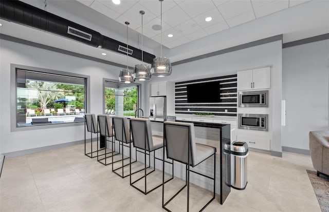 kitchen with baseboards, appliances with stainless steel finishes, decorative light fixtures, a kitchen bar, and white cabinetry