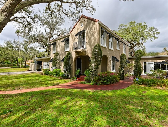 view of front of property featuring a front yard, a tile roof, a balcony, and stucco siding