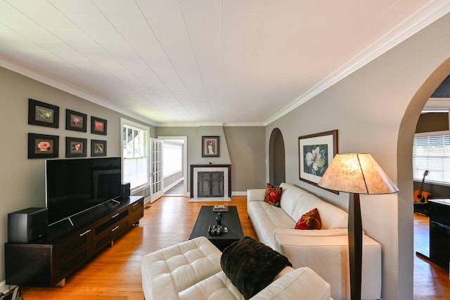 living area featuring light wood-style floors, arched walkways, a healthy amount of sunlight, and crown molding