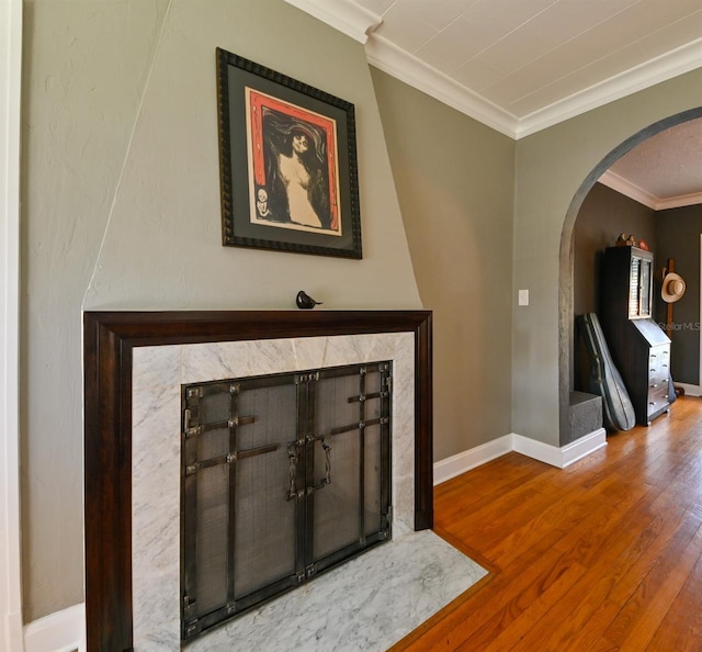 interior details with baseboards, arched walkways, crown molding, and wood finished floors