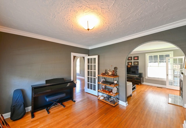 living area featuring arched walkways, french doors, wood-type flooring, ornamental molding, and a textured ceiling