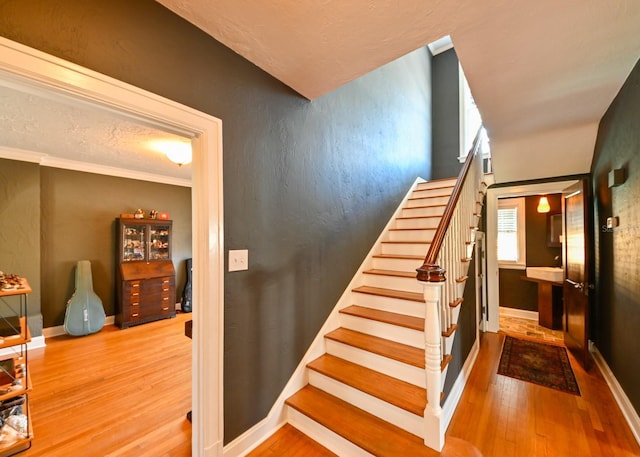 stairway with ornamental molding, baseboards, and wood finished floors