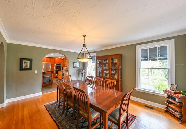 dining space with arched walkways, light wood-style flooring, and visible vents