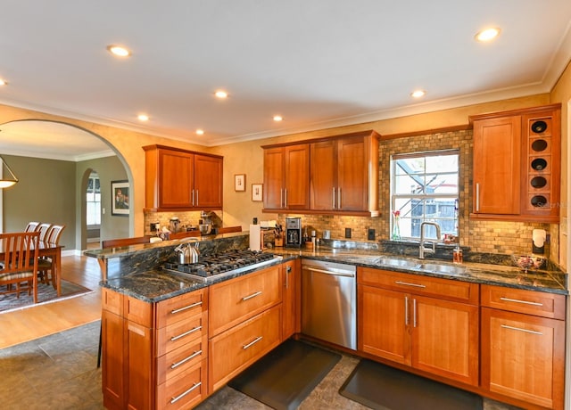 kitchen with arched walkways, brown cabinets, stainless steel appliances, a sink, and a peninsula