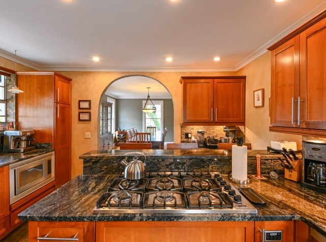 kitchen with appliances with stainless steel finishes, arched walkways, ornamental molding, and dark stone countertops