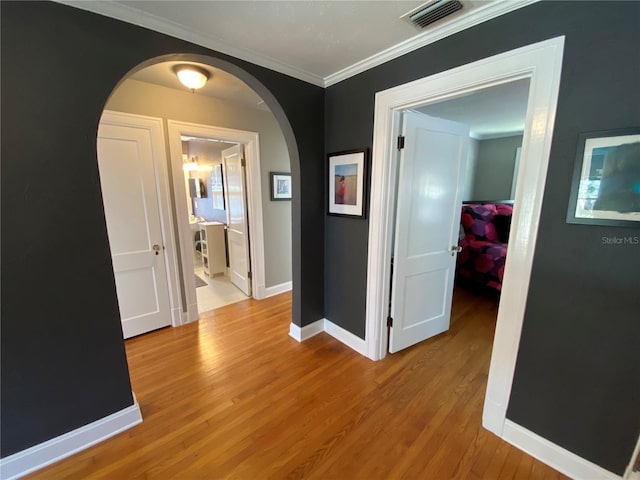 hallway with arched walkways, visible vents, baseboards, light wood-style floors, and ornamental molding