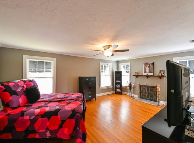 bedroom featuring a textured ceiling, light wood-style flooring, a ceiling fan, baseboards, and a brick fireplace