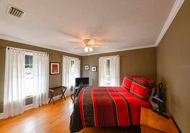 bedroom featuring light wood-style floors, visible vents, crown molding, and ceiling fan