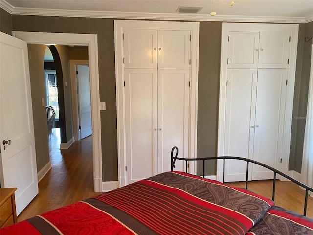 bedroom with crown molding, arched walkways, and wood finished floors