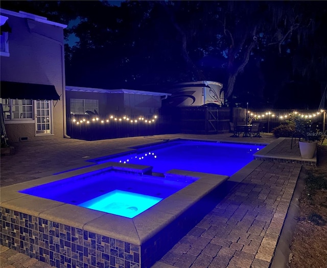 pool at night featuring a fenced in pool, a patio area, and an in ground hot tub