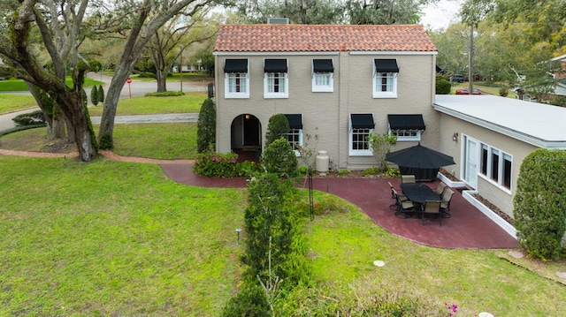 view of front facade with a patio, a front yard, a tile roof, and stucco siding