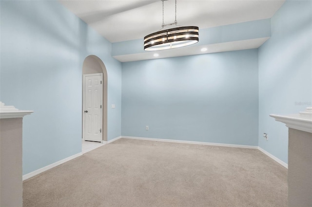 carpeted empty room featuring arched walkways and baseboards