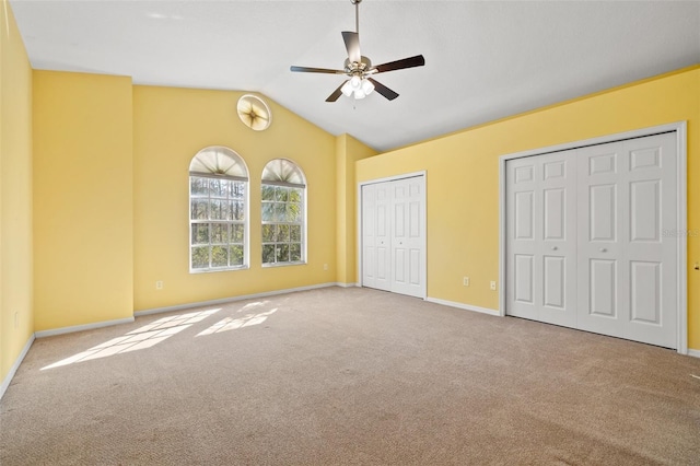 unfurnished bedroom with two closets, lofted ceiling, carpet flooring, ceiling fan, and baseboards