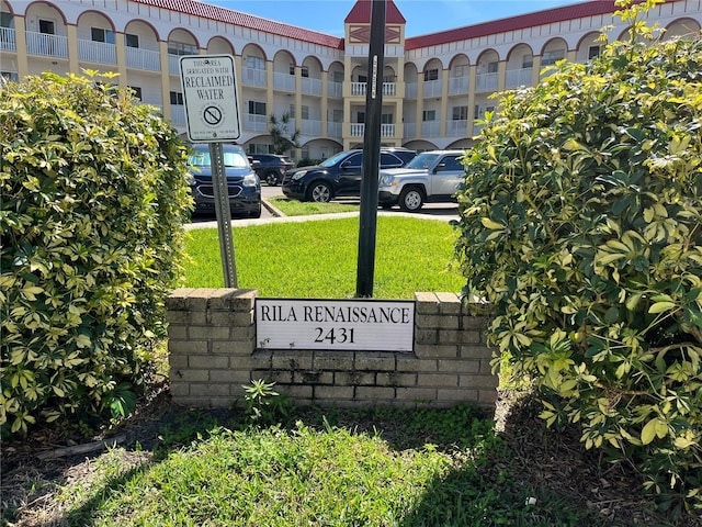 community / neighborhood sign featuring uncovered parking and a lawn