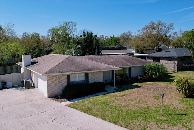 ranch-style home with driveway, brick siding, an attached garage, central AC, and a front yard