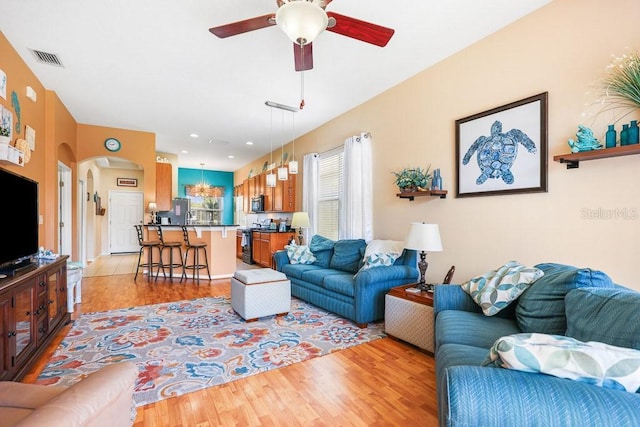 living area with light wood-style floors, arched walkways, visible vents, and a ceiling fan