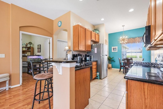 kitchen with arched walkways, a breakfast bar, a peninsula, black appliances, and a sink