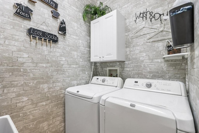 washroom featuring brick wall, washing machine and dryer, and cabinet space