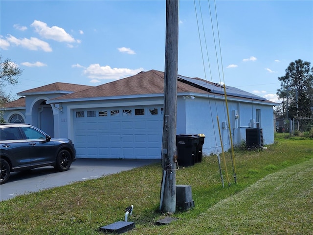 view of side of home with solar panels, an attached garage, a yard, central AC, and stucco siding