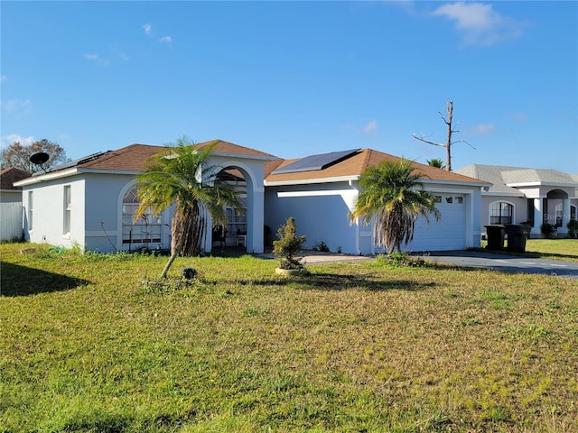 single story home featuring a garage, a front yard, solar panels, and stucco siding