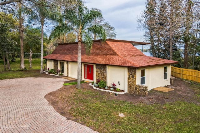 view of front of house with a shingled roof, fence, stone siding, decorative driveway, and stucco siding