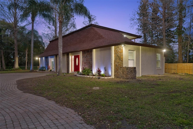 view of front of home with a yard, stone siding, fence, and stucco siding