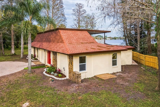 view of property exterior with driveway, roof with shingles, fence, and stucco siding