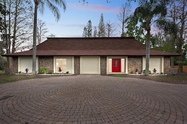 view of front of home featuring stone siding, curved driveway, roof with shingles, and stucco siding