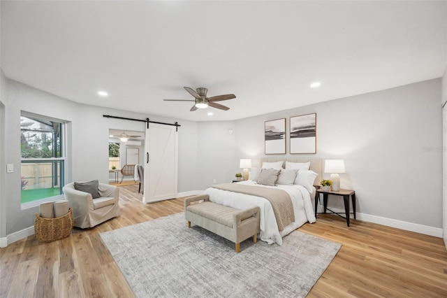 bedroom with a barn door, light wood-type flooring, recessed lighting, and baseboards