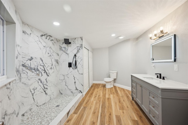 bathroom with a marble finish shower, baseboards, toilet, wood finished floors, and vanity