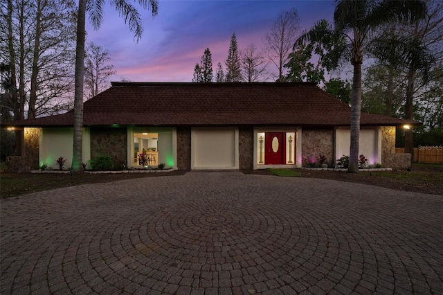 view of front of property with stone siding, curved driveway, and stucco siding