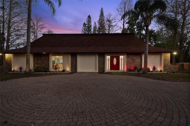 view of front of house with stone siding, roof with shingles, curved driveway, and stucco siding