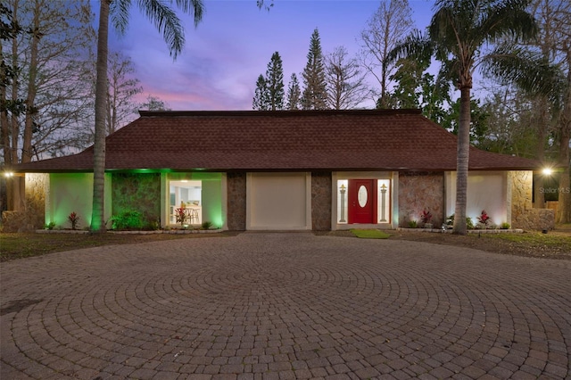 view of front of house featuring stone siding, a shingled roof, and curved driveway