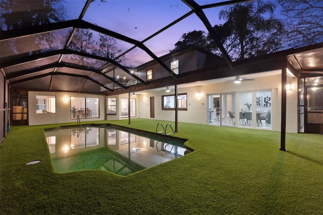 view of pool with glass enclosure, a ceiling fan, a lawn, and a patio