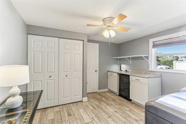 kitchen featuring beverage cooler, light countertops, a textured ceiling, light wood-style floors, and open shelves