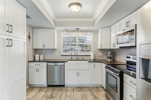 kitchen with stainless steel appliances, a raised ceiling, visible vents, ornamental molding, and a sink