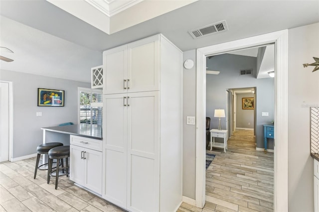 kitchen with a breakfast bar, white cabinets, visible vents, and light wood finished floors