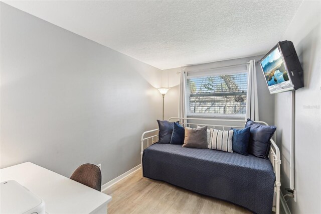 living area featuring a textured ceiling, light wood-style flooring, and baseboards