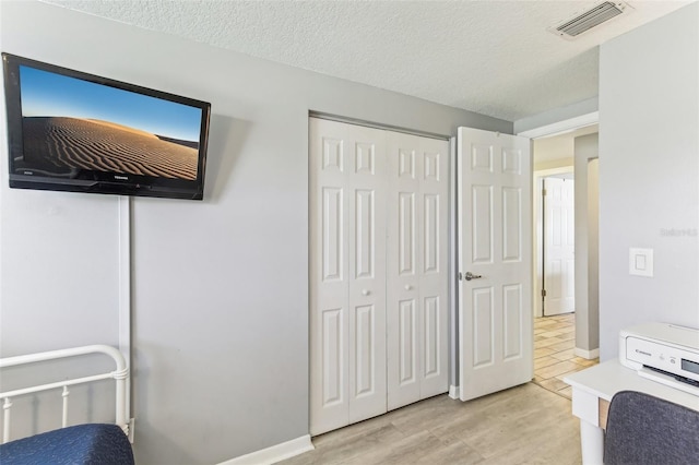 bedroom with a closet, visible vents, light wood-style flooring, a textured ceiling, and baseboards