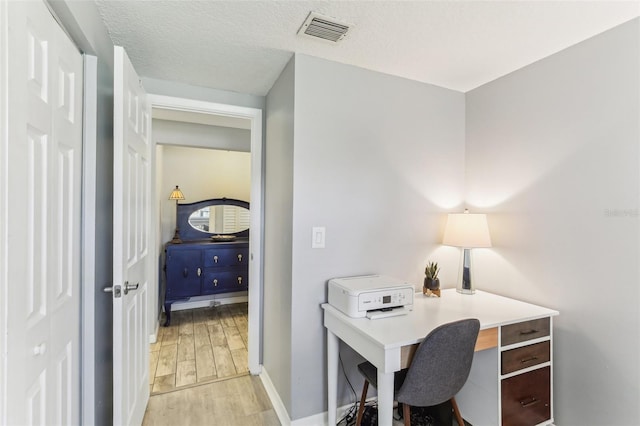 office space with light wood-type flooring, visible vents, a textured ceiling, and baseboards