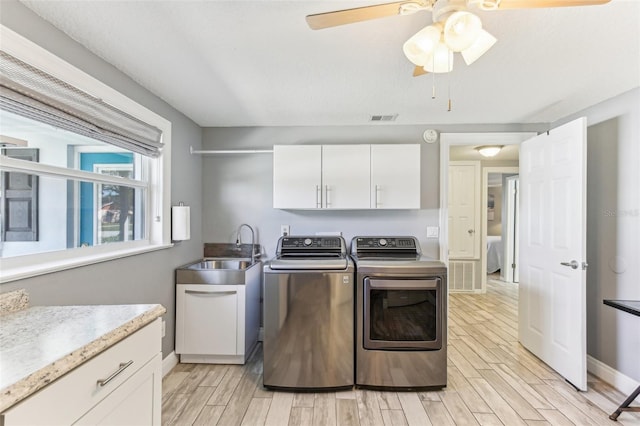 laundry area featuring wood finish floors, cabinet space, visible vents, a sink, and washer and dryer