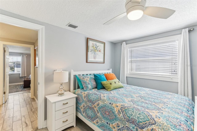 bedroom with light wood finished floors, ceiling fan, visible vents, and a textured ceiling