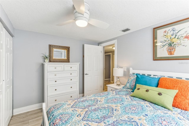 bedroom with light wood finished floors, a textured ceiling, visible vents, and a closet