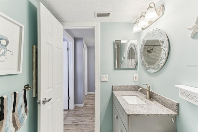 bathroom with a textured ceiling, wood finish floors, vanity, visible vents, and baseboards