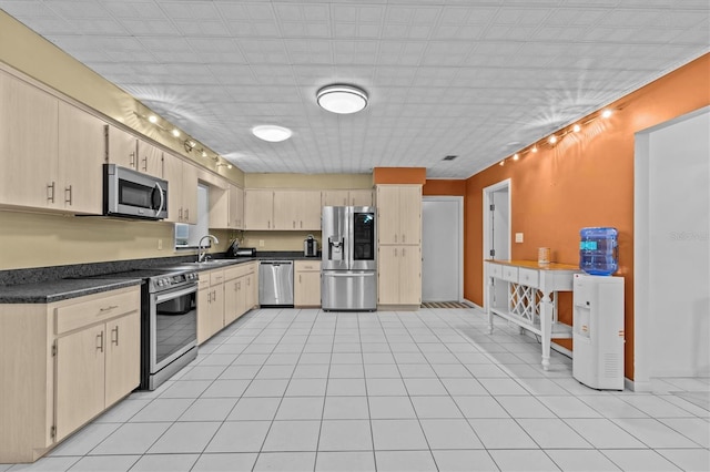 kitchen featuring light tile patterned floors, dark countertops, light brown cabinetry, appliances with stainless steel finishes, and a sink