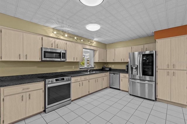 kitchen featuring appliances with stainless steel finishes, dark countertops, a sink, and light brown cabinetry