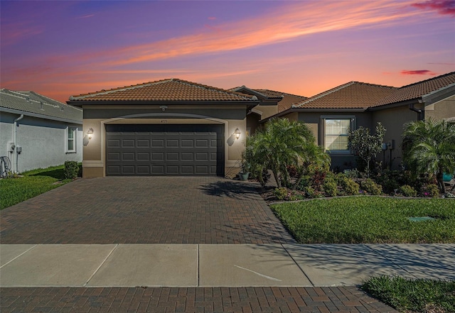 mediterranean / spanish house with a garage, a tiled roof, decorative driveway, and stucco siding