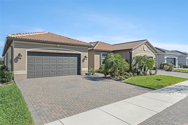 view of front of house with decorative driveway, a tiled roof, an attached garage, and stucco siding